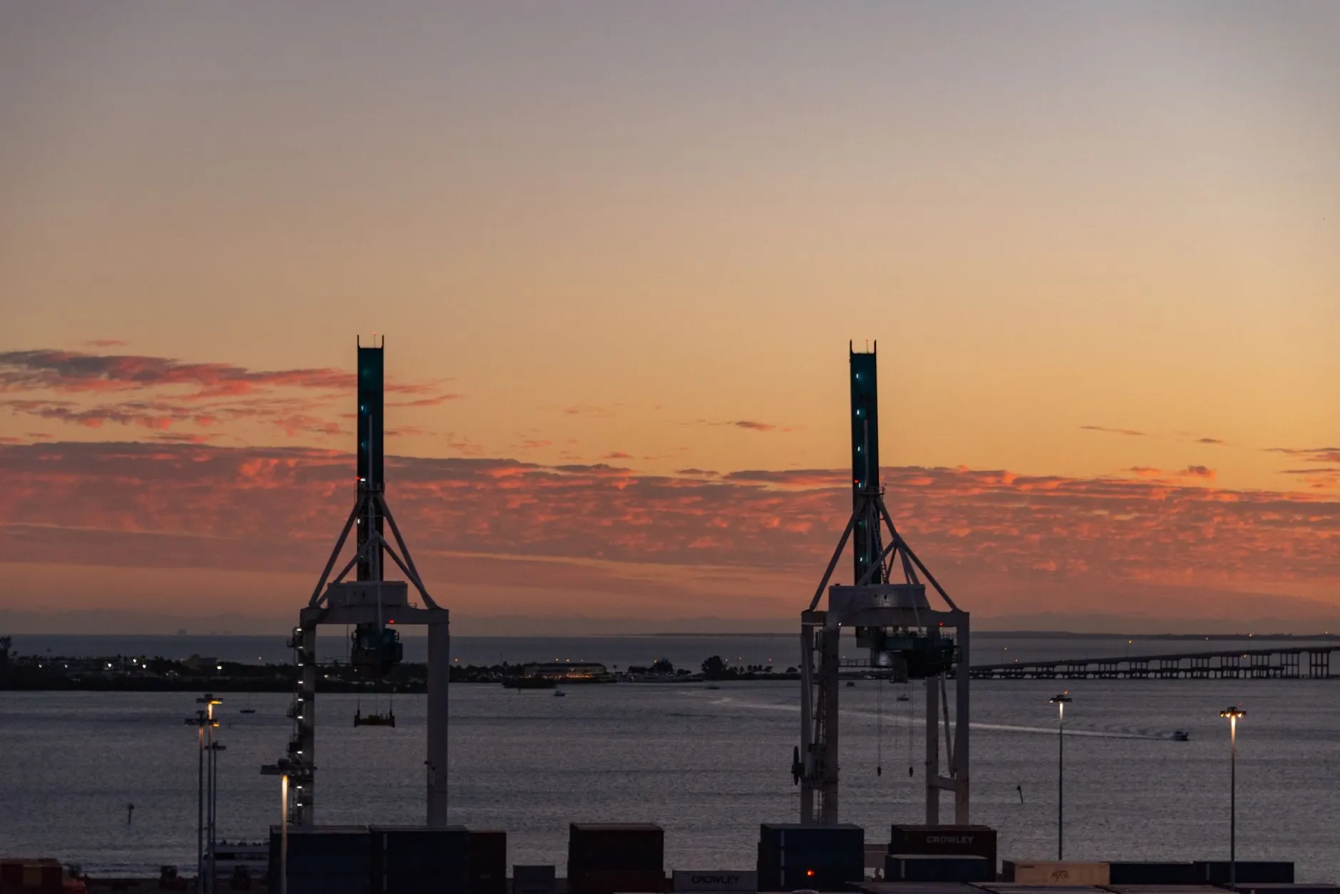 Two container cranes in silhouette against an orange evening sky over the water
