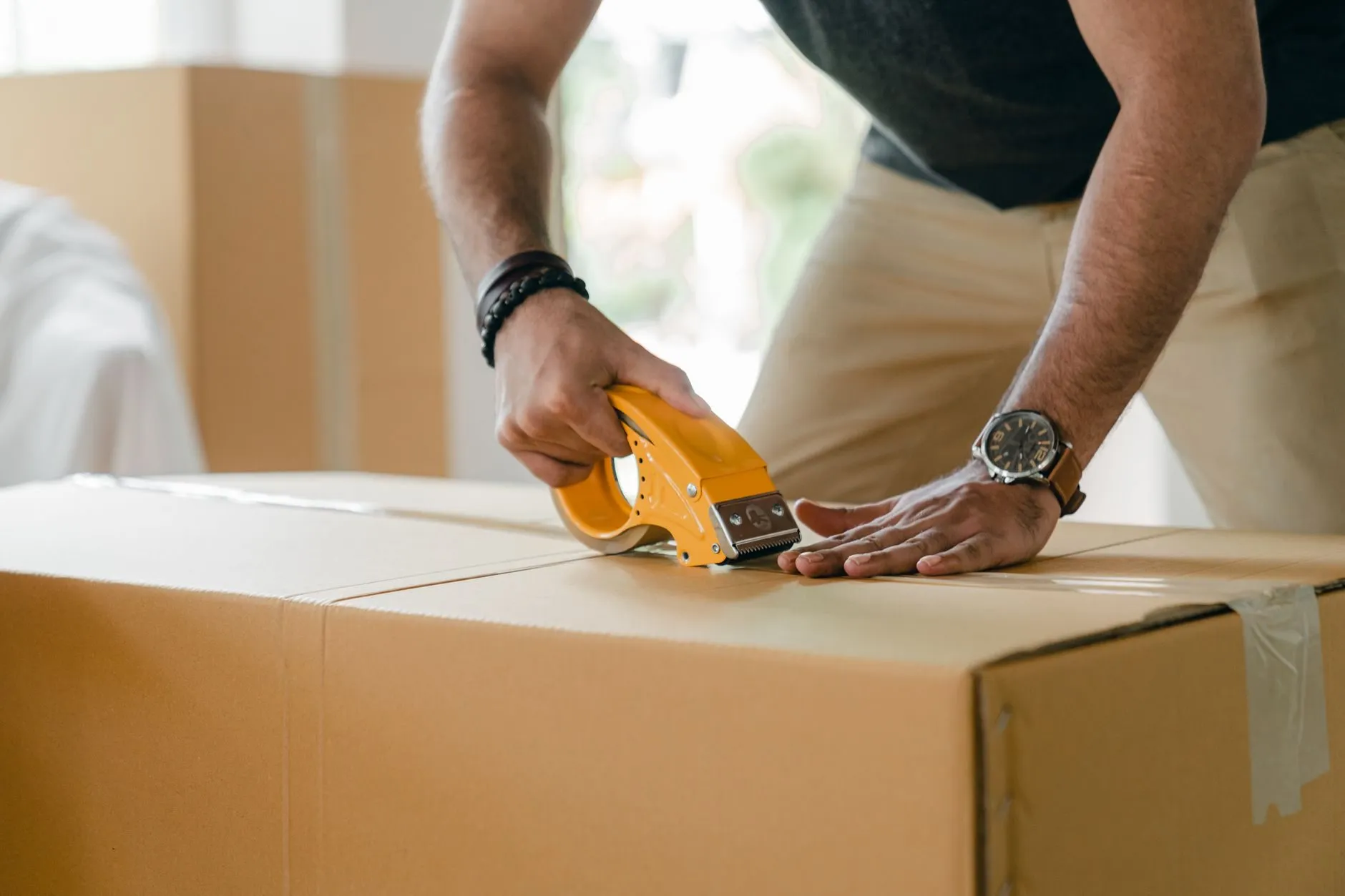 Hands sealing a large cardboard box with a tape dispenser